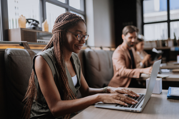 Beautiful businesswoman working on laptop in modern office. Group of freelancers working in shared work area. Concept of coworking, common workspaces for business, startups. Working remotely from coffee shop.