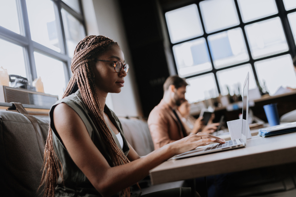 Beautiful businesswoman working on laptop in modern office. Group of freelancers working in shared work area. Concept of coworking, common workspaces for business, startups. Working remotely from coffee shop.