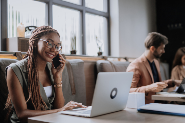 Beautiful businesswoman making phone call in modern office. Group of freelancers working in shared work area. Concept of coworking, common workspaces for business, startups. Working remotely from coffee shop.