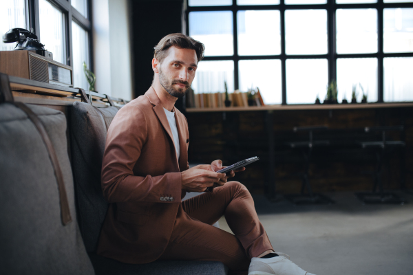 Handsome businessman preparing for meeting, working on presentation on tablet, sitting in modern office. Working remotely from coffee shop.