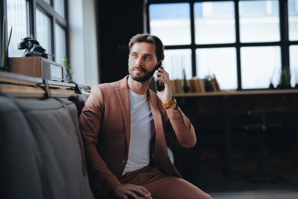 Handsome businessman preparing for meeting, making call from smartphone, sitting in modern office. Working remotely from coffee shop.