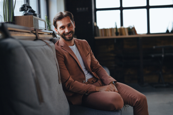 Portrait of handsome businessman in suit sitting in modern office, smiling, looking at camera. Working remotely from coffee shop.