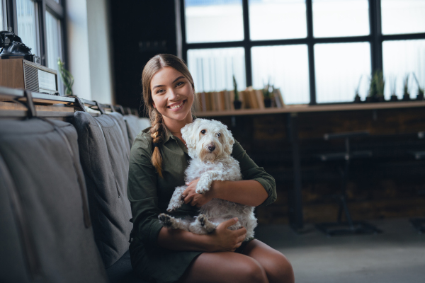 Portrait of beautiful young woman holding her dog and smiling. Cute white dog in arms of loving owner. With dog in coffe shop.