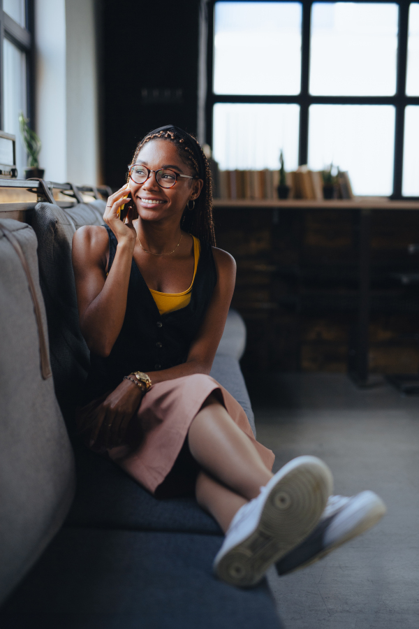 Portrait of beautiful woman sitting in modern office and making phone call, smiling. Working remotely from the coffee shop, relaxed atmosphere.