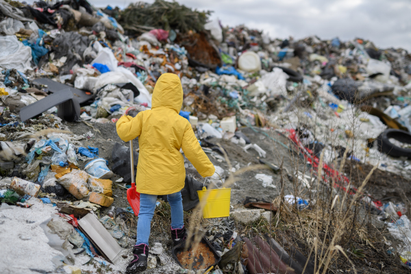 Young girl picking up litter, debris along riverbank in nature. Water and environmental pollution, future generations, eco activism concept.