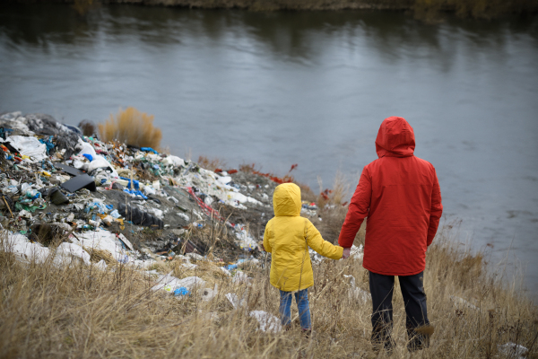 Young girl among eco activists picking up litter along riverbank, in nature, environmental pollution, eco activism and plogging concept.