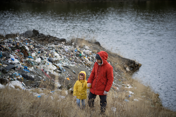 Young girl among eco activists picking up litter along riverbank, in nature, environmental pollution, eco activism and plogging concept.