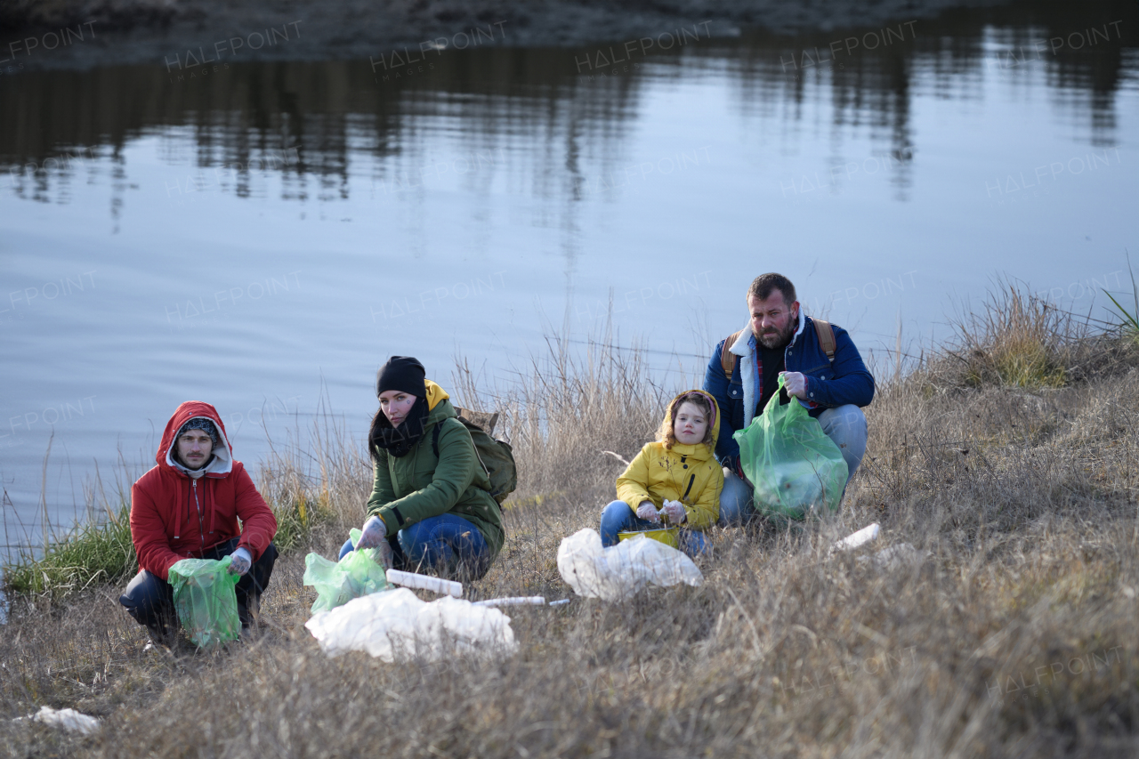 Young girl among eco activists picking up litter along riverbank, in nature, environmental pollution, eco activism and plogging concept.