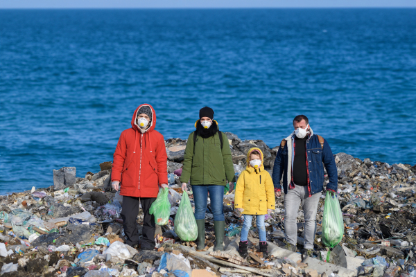 Young girl among eco activists standing on coastline, shore of sea. Environmental pollution, eco activism and plogging concept. Greta lookalike.