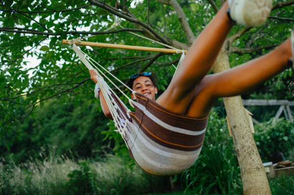 Yong teenage girl outdoors in garden, swinging on swing, having fun during warm summer evening.