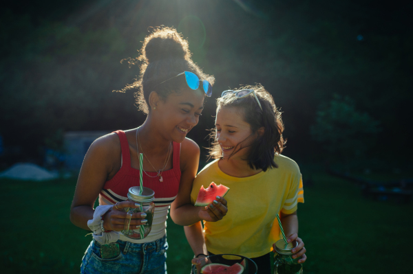 Cheerful young teenager girls friends outdoors in garden, eating watermelon.