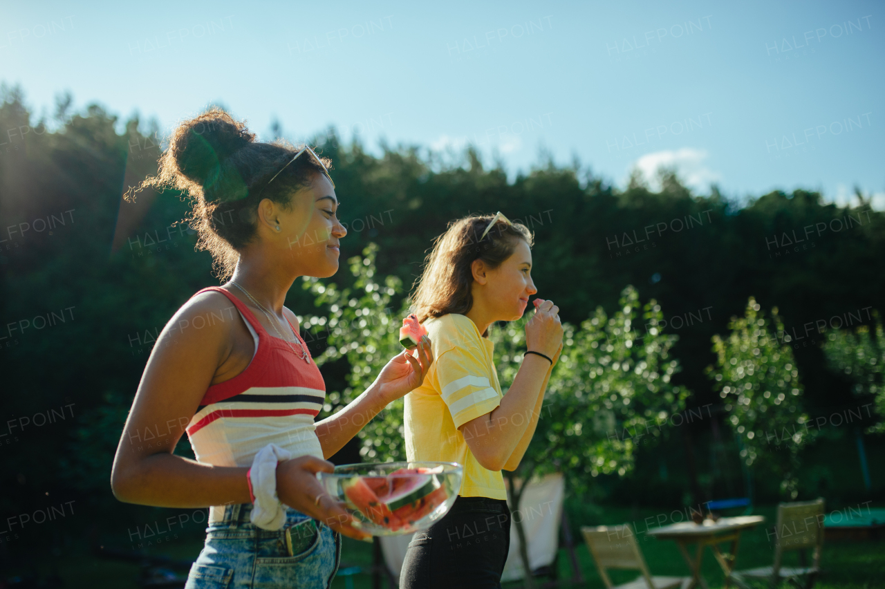 Cheerful young teenager girls friends outdoors in garden, eating watermelon.