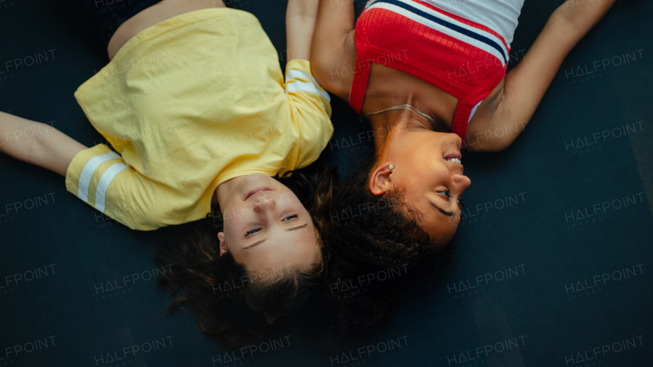 Teenager girls friends spending time outdoors in garden, laughing. Top view, lying on trampoline during summer day. Best friends forever.