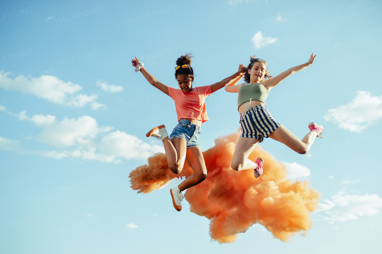 Low angle view of young teenager girls friends jumping high. Having fun outdoors in city, standing on concrete wall.