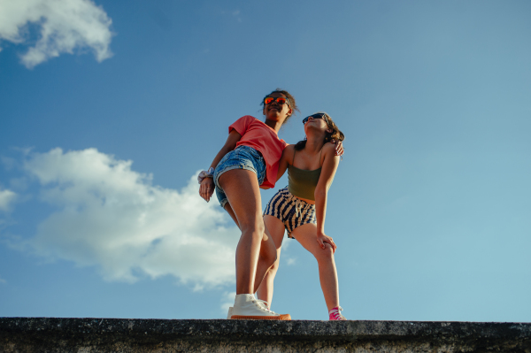 Low angle view of young teenager girls friends outdoors in city, standing on concrete wall.