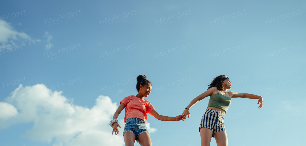 Low angle view of young teenager girls friends outdoors in city, standing on concrete wall. Summer banner with copyspace.