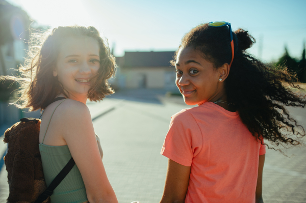 Rear view of teenager girls friends with skateboards walking outdoors in city.