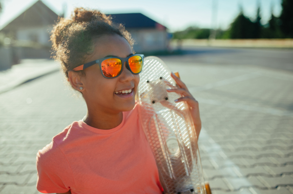 Young teenager girl with skateboards spending time outdoors in city during warm summer holiday day. Sitting on parking lot.