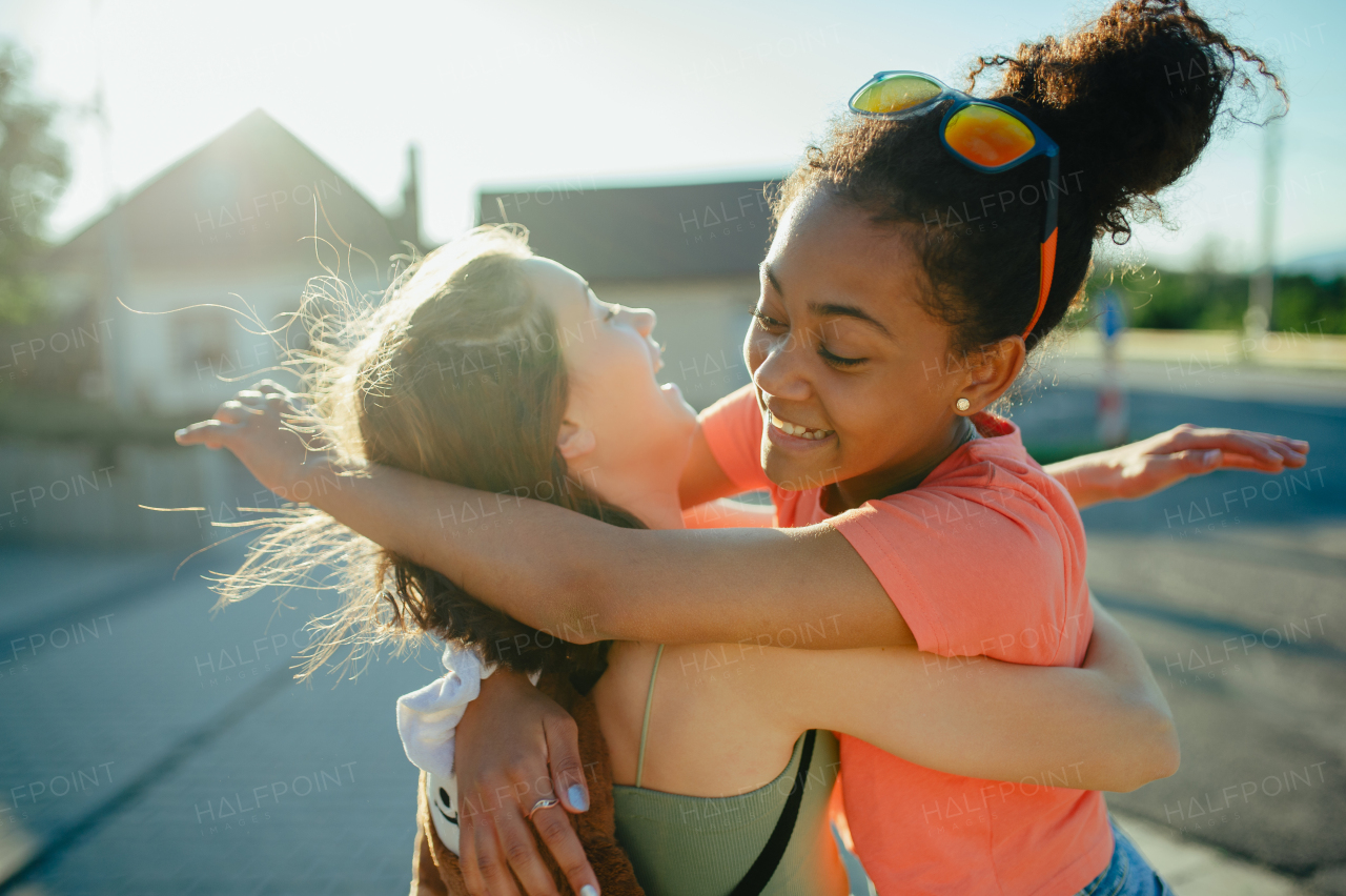 Young teenager girl best friends greeting each other, hugging. Girls spending time outdoors in city during warm summer holiday day.