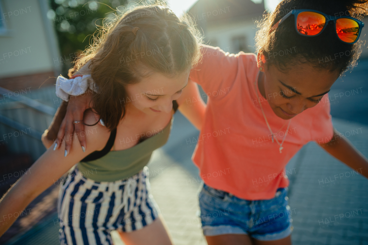 Young teenager girl best friends greeting each other, hugging. Girls spending time outdoors in city during warm summer holiday day.