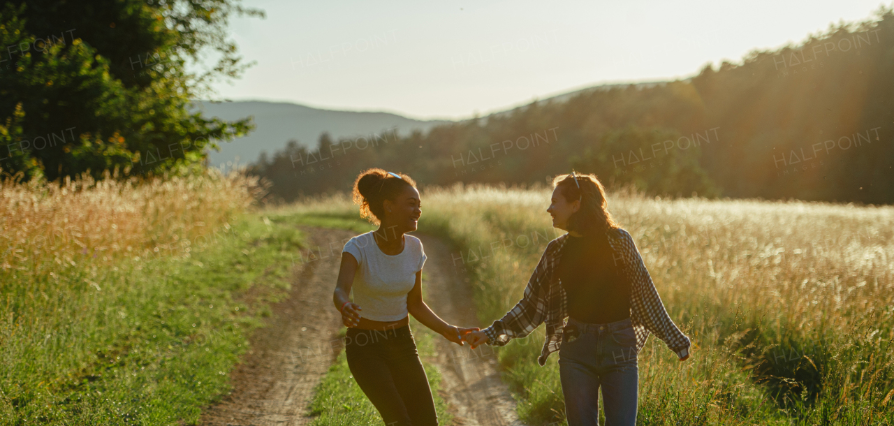 Cheerful young teenager girl best friends spending time in nature, during sunset. Girls on walk by forest, summer holidays. Banner with copyspace.