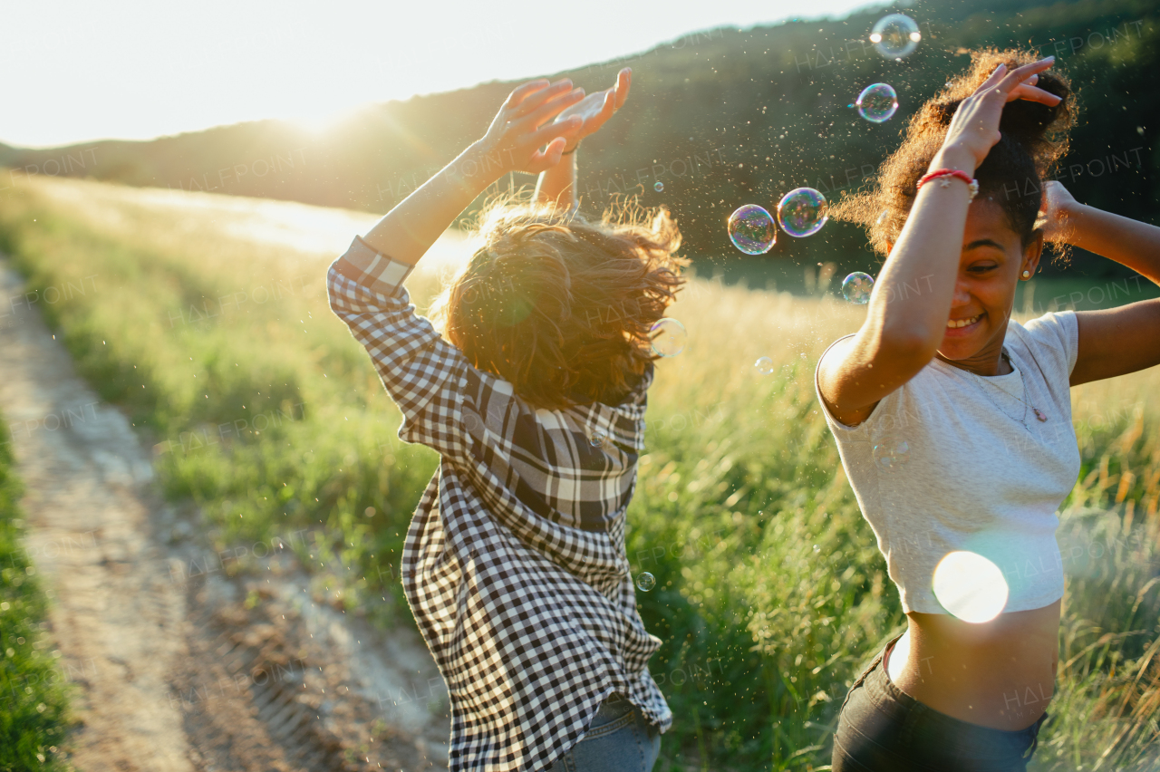 Cheerful young teenager girl best friends spending time in nature, during sunset. Girls blowing bubbles and popping them.