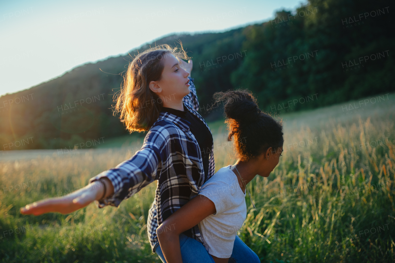 Cheerful young teenager girl best friends spending time in nature, during sunset. Girls on walk, carrying each other on back.