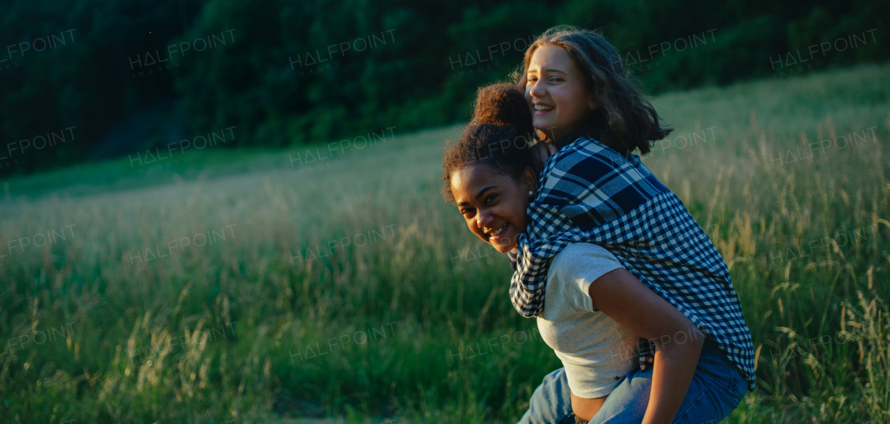 Cheerful young teenager girl best friends spending time in nature, during sunset. Girls on walk, carrying each other on back.