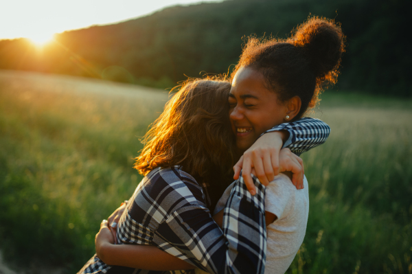 Cheerful young teenager girl best friends spending time in nature, during sunset. Girls on walk, embracing.