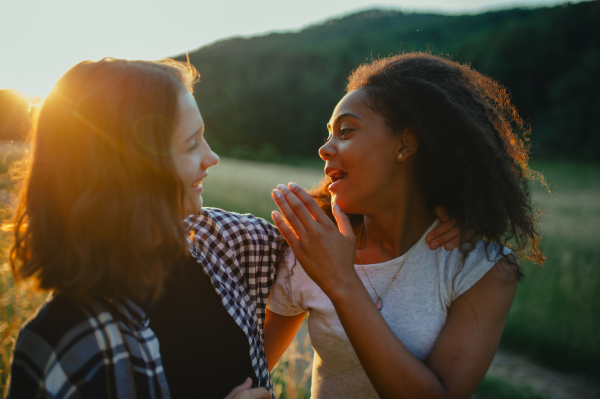 Cheerful young teenager girl best friends spending time in nature, during sunset. Girls on walk, embracing.