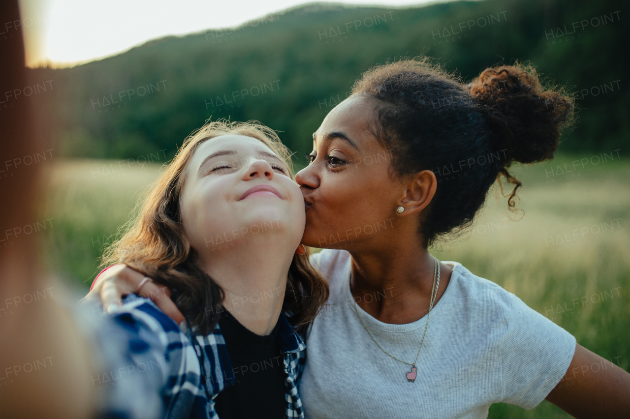 Cheerful young teenager girl best friends spending time in nature, during sunset. Girls on walk, taking selfie with smartphone.