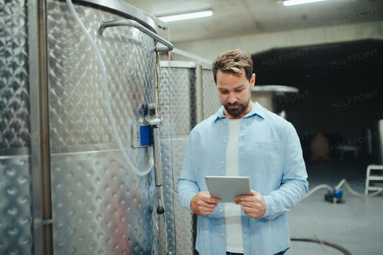 The winemaker standing in the wine cellar, monitoring the fermentation and aging processes in large barrels, holding clipboard.