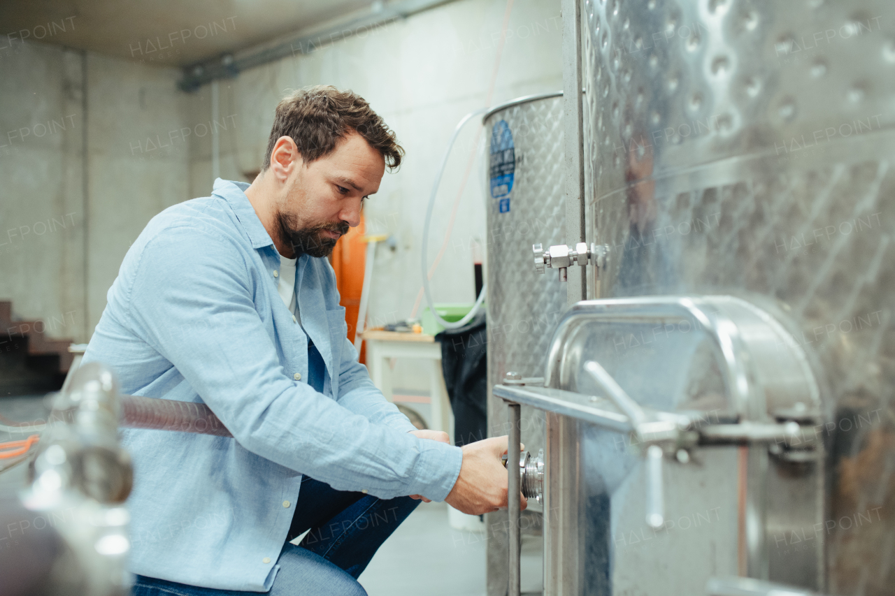 Winemaker standing in the wine cellar, controlling pressure in fermentation tank