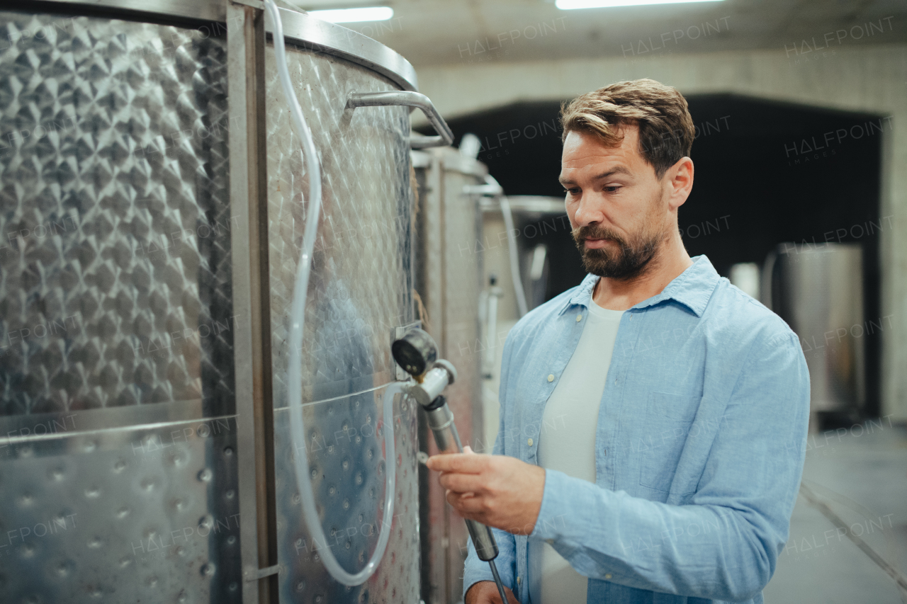 Winemaker standing in the wine cellar, controlling pressure in fermentation tank