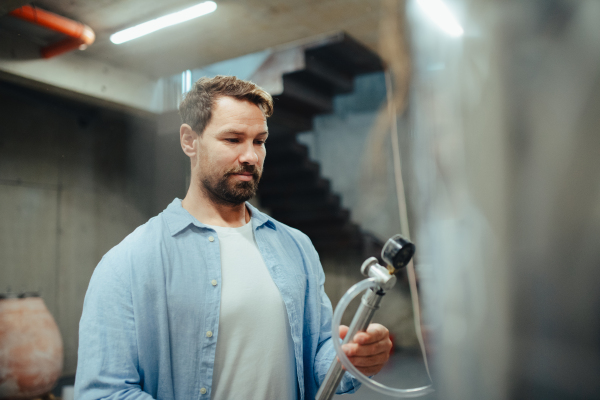 Winemaker standing in the wine cellar, controlling pressure in fermentation tank