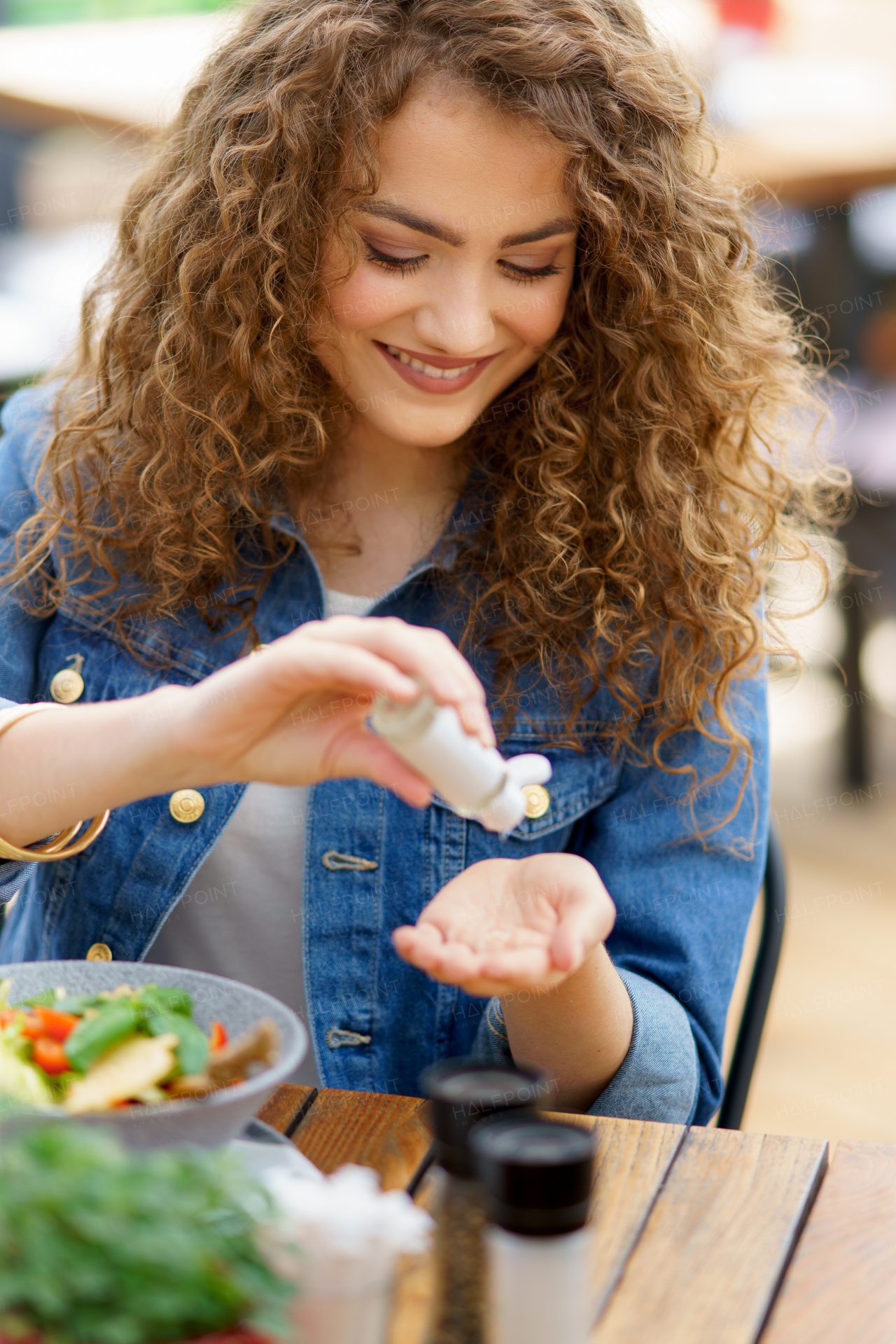 Beautiful woman sanitizing her hands with disinfectant gel in a restaurant before eating. Having lunch or brunch outdoors in restaurant patio.