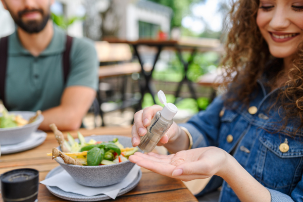 Beautiful woman sanitizing her hands with disinfectant gel in a restaurant before eating. Having lunch or brunch outdoors in restaurant patio.