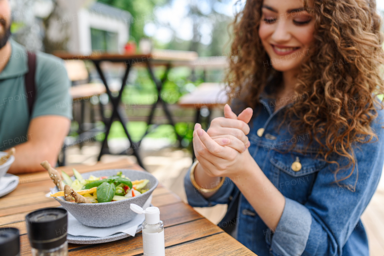 Beautiful woman sanitizing her hands with disinfectant gel in a restaurant before eating. Having lunch or brunch outdoors in restaurant patio.