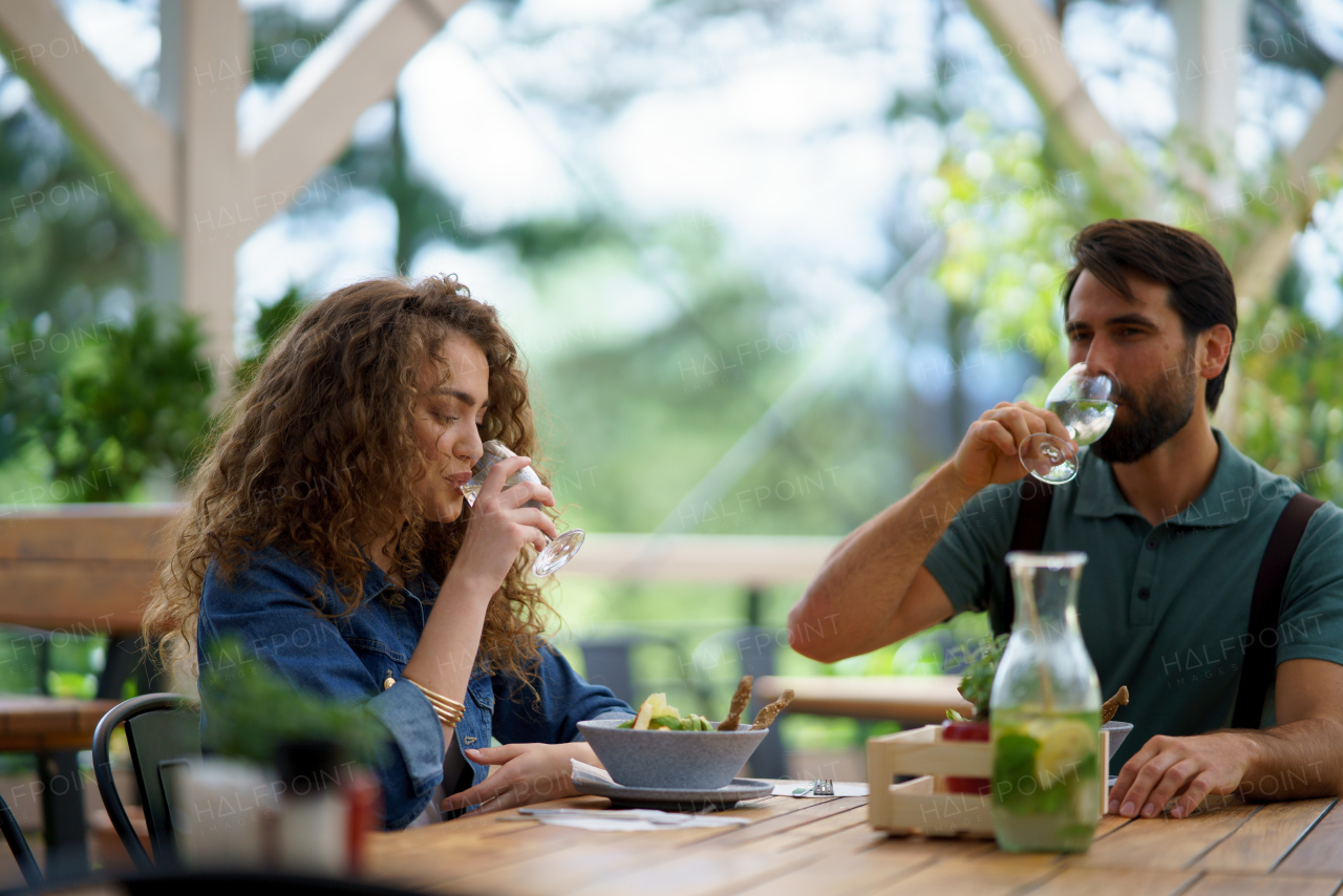 Young couple at date in restaurant, sitting on restaurant terrace, drinking water. Boyfriend and girlfriend enjoying springtime, having lunch or brunch outdoors, outdoor seating for dining.