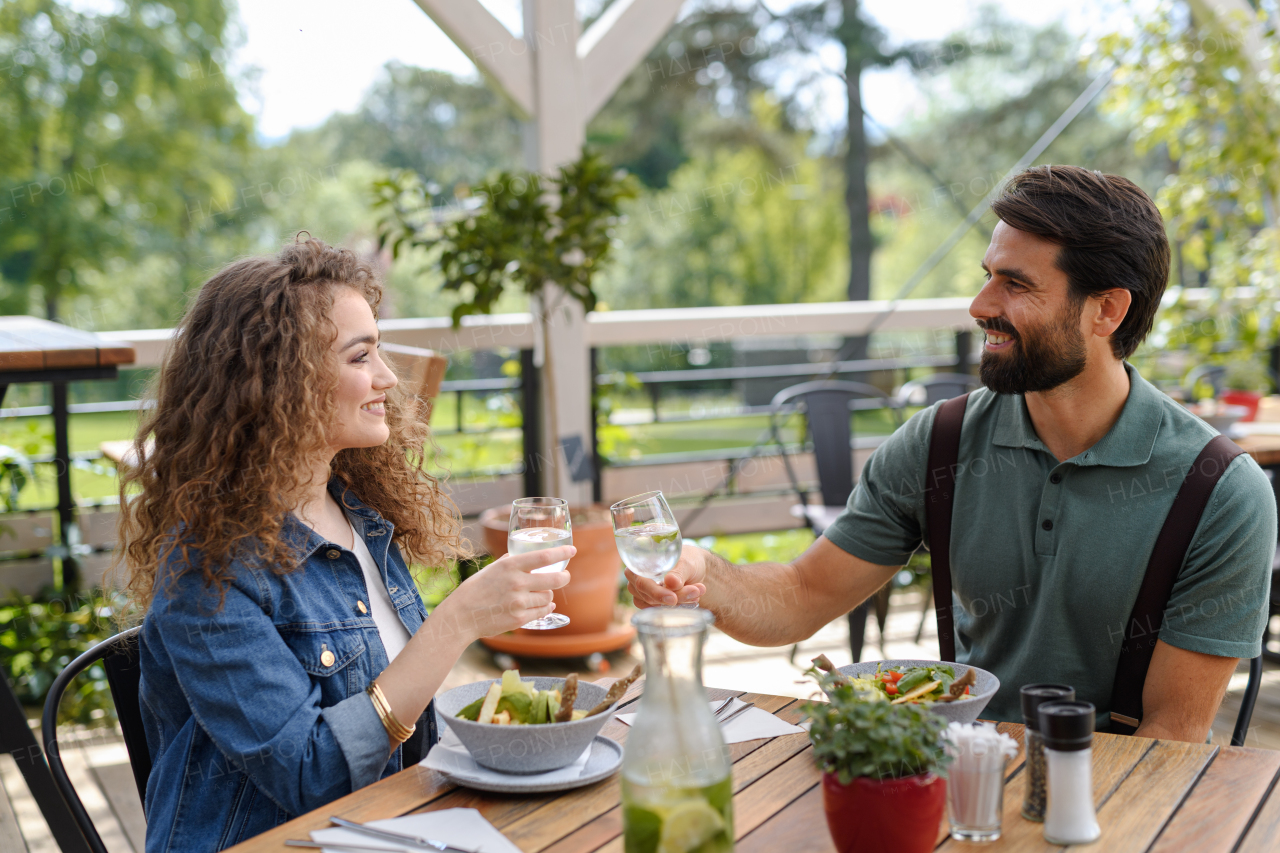 Young couple at date in restaurant, sitting on restaurant terrace. Boyfriend and girlfriend enjoying springtime, having lunch or brunch outdoors, outdoor seating for dining.