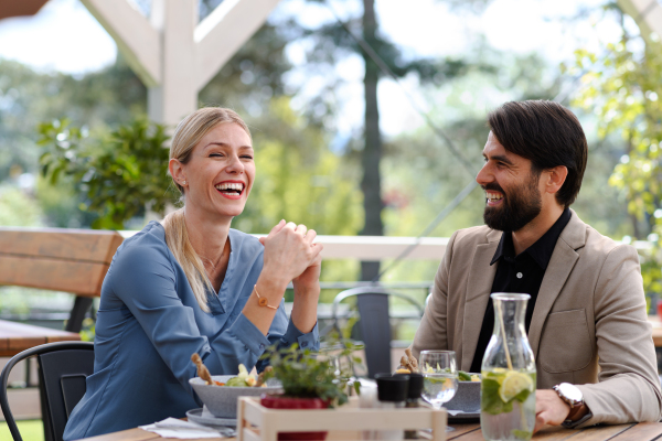 Couple sitting outdoors on terrace restaurant, having romantic dinner date, laughing. Business lunch for two managers, discussing new business project.