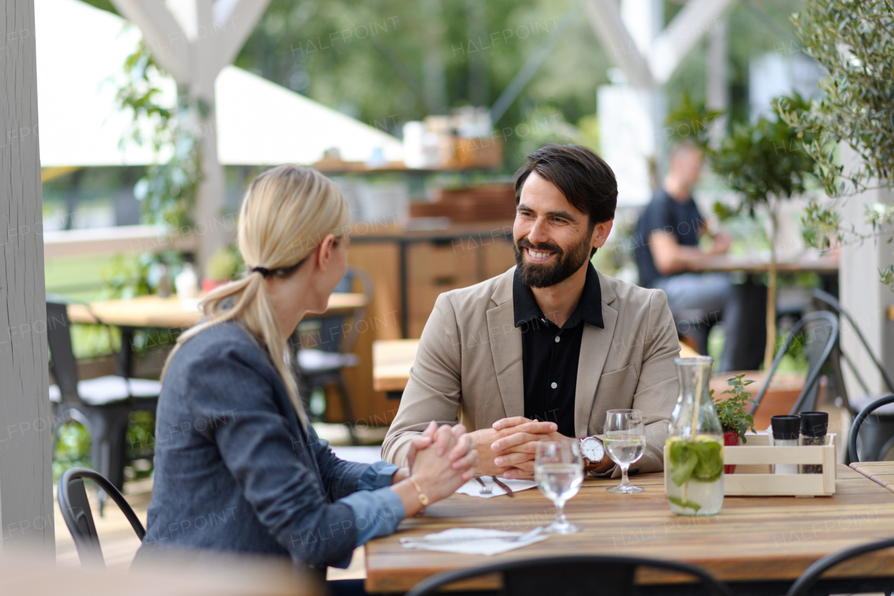 Couple sitting outdoors on terrace restaurant, having romantic dinner date. Business lunch for two managers, discussing new business project.