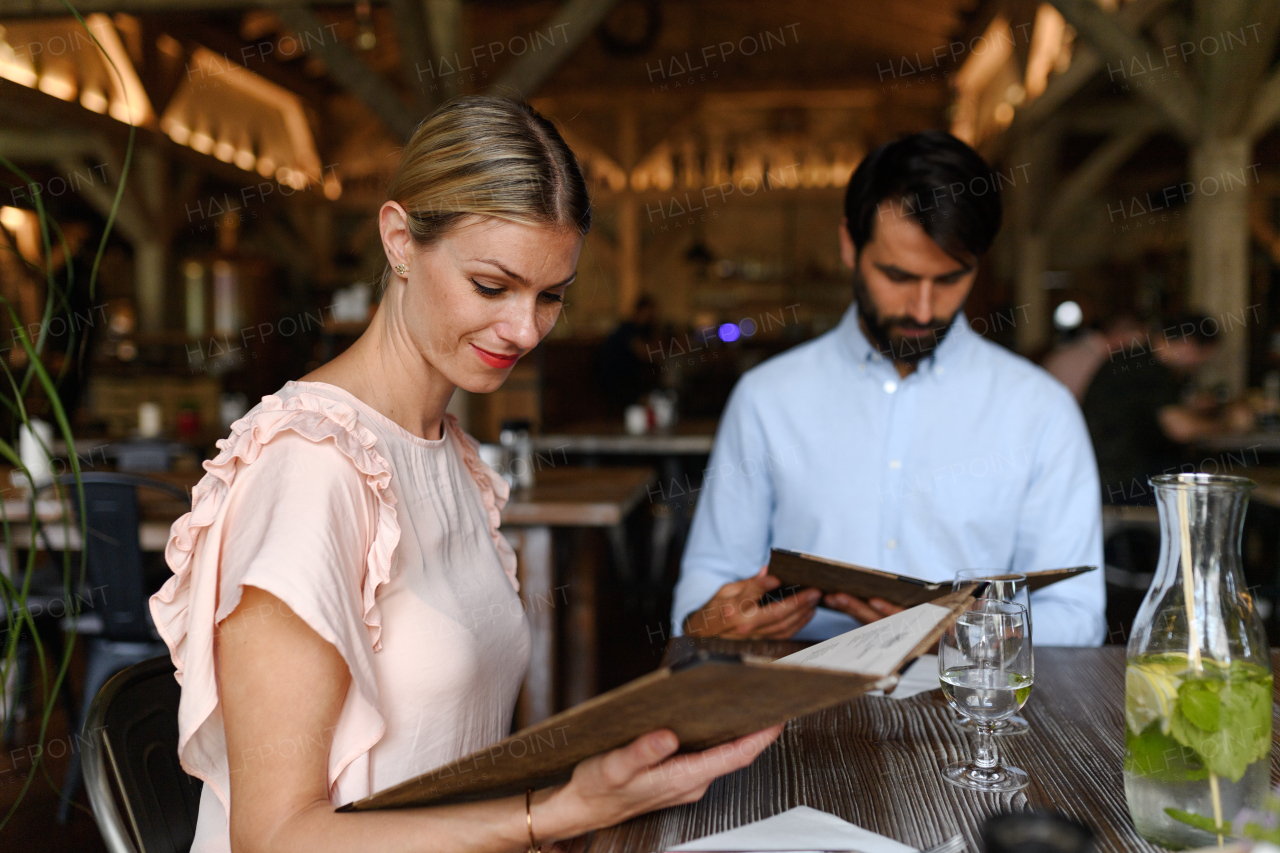 Husband and wife choosing food from menu. Happy loving couple at date in restaurant, having brunch, lunch in modern cafe.