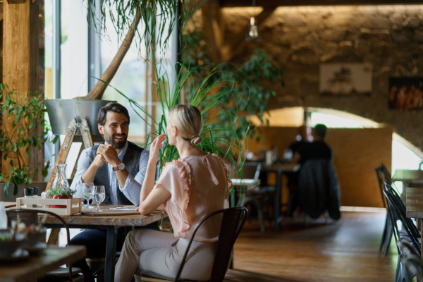 Happy loving couple at date in restaurant. Husband and wife sitting at table, laughing, having brunch, lunch in modern cafe.