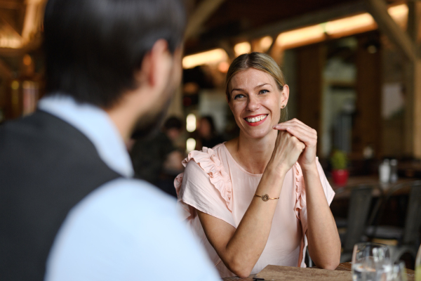 Happy loving couple at date in restaurant. Husband and wife sitting at table, laughing, having brunch, lunch in modern cafe.