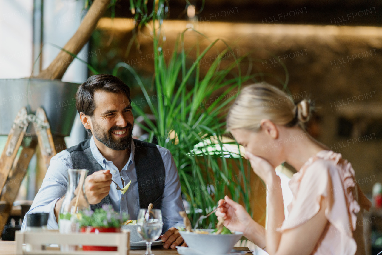 Happy loving couple at date in restaurant. Husband and wife sitting at table, laughing, having brunch, lunch in modern cafe.