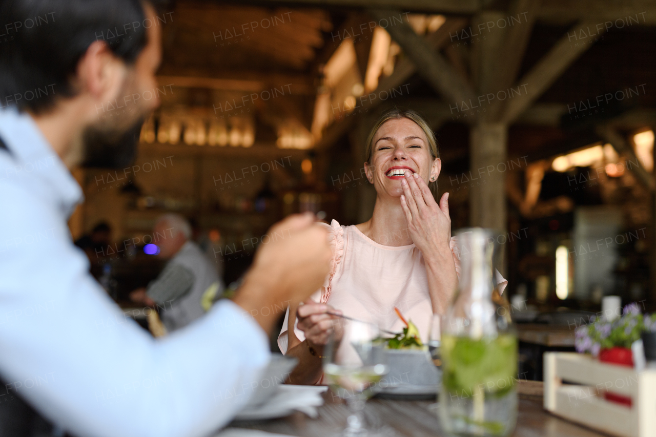 Happy loving couple at date in restaurant. Husband and wife sitting at table, laughing, having brunch, lunch in modern cafe.