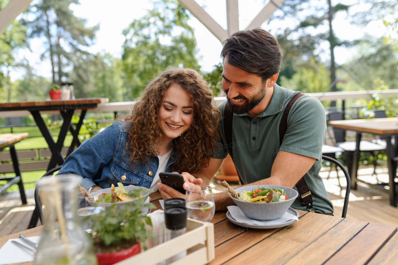 Young couple at date in restaurant, sitting on restaurant terrace. Boyfriend and girlfriend enjoying springtime, having lunch or brunch outdoors, outdoor seating for dining.