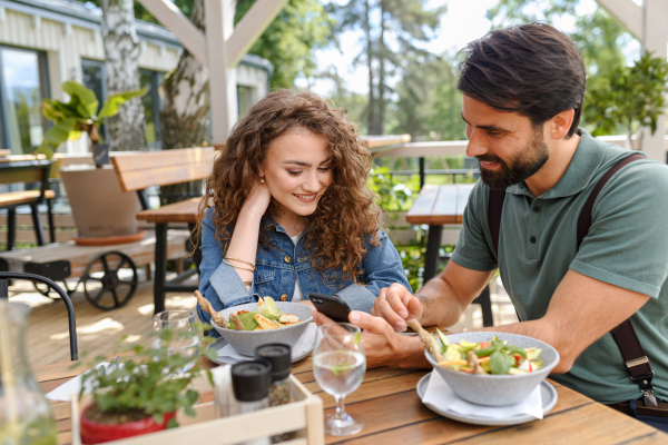 Young couple at date in restaurant, sitting on restaurant terrace. Boyfriend and girlfriend enjoying springtime, having lunch or brunch outdoors, outdoor seating for dining.