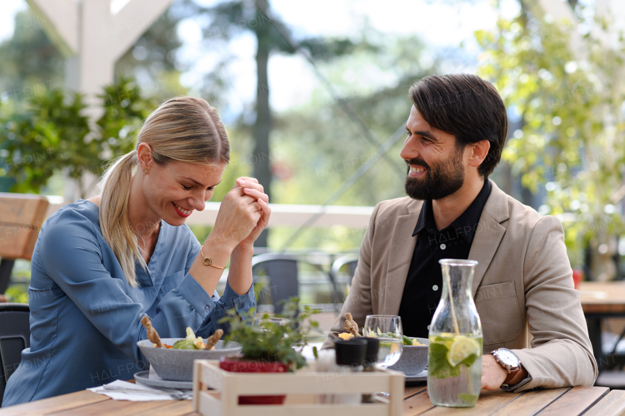 Couple sitting outdoors on terrace restaurant, having romantic dinner date. Business lunch for two managers, discussing new business project.